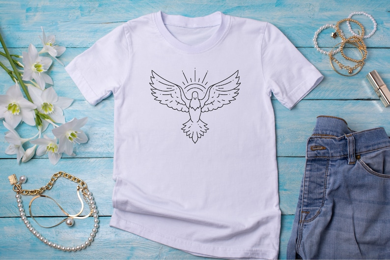 以下が含まれることがあります： 白いTシャツに、黒い線で描かれた、羽を広げた鳩と、その上に輝く太陽のイラストが描かれています。