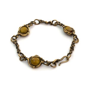 Peut inclure: Un bracelet de style vintage avec quatre pierres ovales de couleur ambre serties dans un métal orné de couleur bronze. Le bracelet présente un design de maillons décoratifs et texturés et un fermoir à crochet. Le bijou est présenté sur fond blanc.