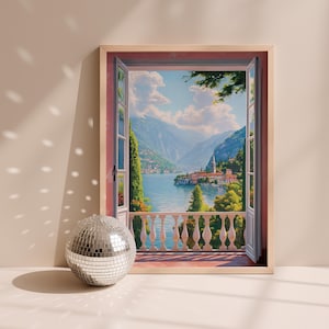 May include: A framed landscape painting depicts a scenic view through an open window. The artwork showcases a serene lake surrounded by mountains and buildings. A silver disco ball sits in front of the frame, reflecting light.