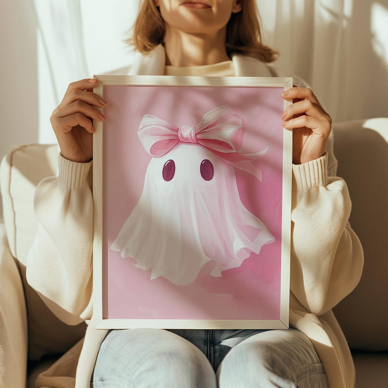May include: A framed illustration of a pink ghost with a pink bow on a pink background.