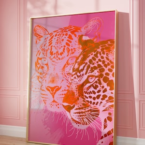 May include: A pink and orange abstract art print featuring two leopards' faces. The leopards are facing each other, with one leopard's face partially obscured by the other. The print is framed in a gold frame.
