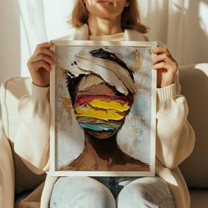May include: A framed painting of a person's face with colorful abstract brushstrokes covering the eyes. The background is a light blue with hints of yellow and pink.