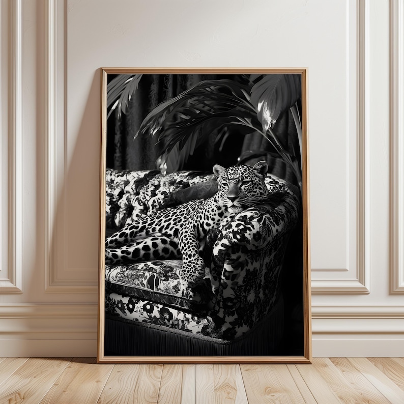 May include: Black and white framed print of a leopard resting on a patterned sofa. The leopard has a spotted coat and is lying down. The sofa has a floral and animal print design. The background includes dark foliage.