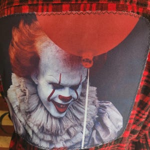 May include: A red and black plaid flannel shirt with a sewn-on patch featuring a close-up of Pennywise the clown from the movie "IT" holding a red balloon.