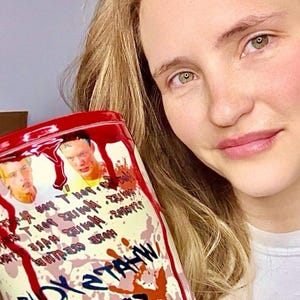May include: A white and red stainless steel tumbler with a bloody handprint design and the text "You Satan" and "Pray For" on the side. The tumbler is held by a person with long blonde hair.