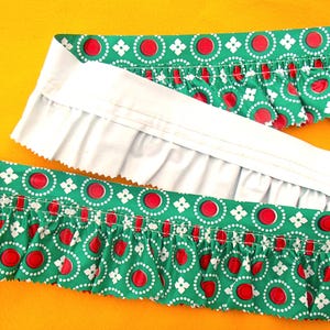 Peut inclure: Tissu à motifs verts et blancs avec des cercles rouges et des accents floraux blancs. Le tissu a un bord à volants et un dos blanc. Le tissu est sur un fond jaune.