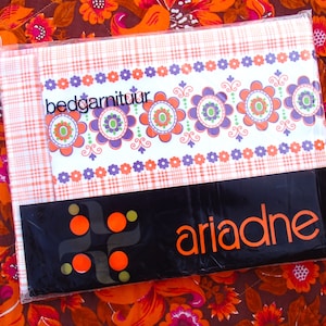 May include: A white and orange bed sheet set with a floral pattern and the text "bedgarnituur" in purple. The packaging is black with the word "ariadne" in orange.