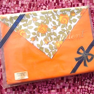 May include: Orange fabric gift wrap with a white floral pattern and blue ribbon. The wrap is packaged in a clear plastic bag and includes a label that reads "Embroidered Set 1 Wash 30°C - 40°C - 1 Scoop All - 15 min - Dress Wash".