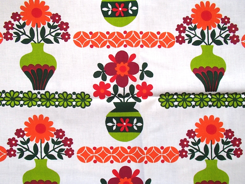 May include: A white fabric with a repeating pattern of green, orange and red flowers in vases. The flowers are stylised and have a retro look. The vases are green with brown and white accents.