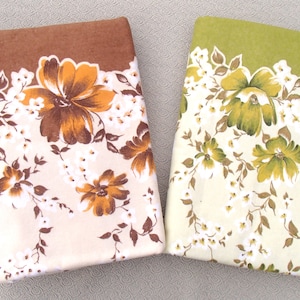 May include: Two folded floral fabric pieces. One is brown with cream and orange flowers, the other is green with cream and yellow flowers. Both have a floral border design.