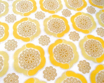 May include: A white fabric with a repeating pattern of yellow and gold stylized flower designs.