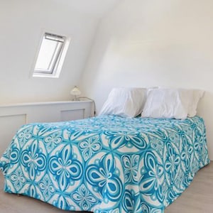 Può includere: Un letto bianco con un copriletto a motivi blu e bianchi. Il letto ha due cuscini bianchi ed è in una stanza bianca con una finestra.