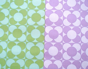 May include: Two fabric swatches with a repeating pattern of stylized flowers. The fabric on the left is light blue with green flowers. The fabric on the right is light purple with white flowers.