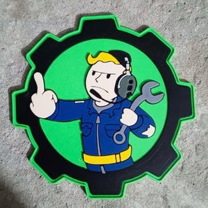 May include: A green and black gear-shaped patch with a cartoon character wearing a blue jumpsuit, headphones, and holding a wrench. The character is giving the middle finger.