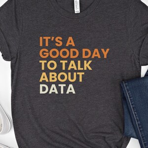 May include: Dark grey heather t-shirt with the text "It's a good day to talk about data" in orange and yellow lettering.