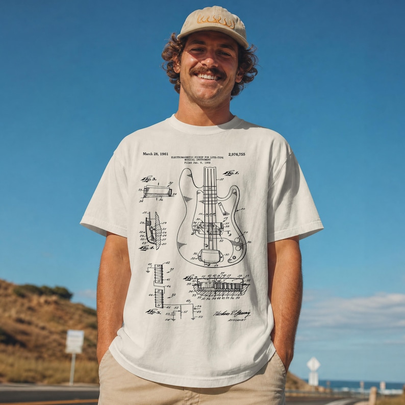 Puede incluir: Camiseta de color crema con un diagrama en blanco y negro de una guitarra el&eacute;ctrica. La camiseta incluye texto que indica una fecha de patente del 28 de marzo de 1961. La persona de la imagen lleva una gorra de b&eacute;isbol beige.