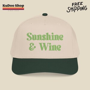 Puede incluir: Gorra de béisbol con corona color crema y visera verde oscuro. La gorra presenta el texto bordado "Sunshine & Wine" en verde. La gorra tiene un botón verde oscuro en la parte superior. El logotipo de KUDOO SHOP está en la esquina superior izquierda.