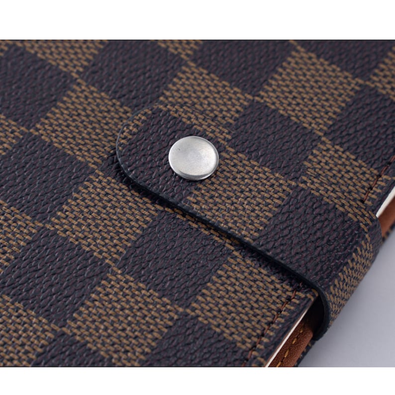 May include: Close-up of a brown and black checkered notebook cover with a silver button.