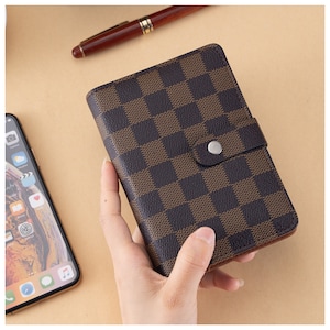 May include: A brown and black checkered leather wallet with a silver button closure.