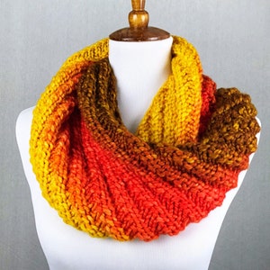 May include: A knitted infinity scarf in shades of yellow, orange, and brown. The scarf is made with a textured stitch and has a gradient color pattern.