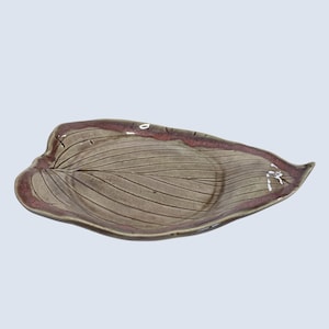 May include: A ceramic leaf-shaped serving dish with a brown and pink glaze. The dish has a raised, textured design that resembles the veins of a leaf.