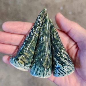 May include: Three ceramic cones with a green and white glaze. The cones are arranged in a triangle shape.