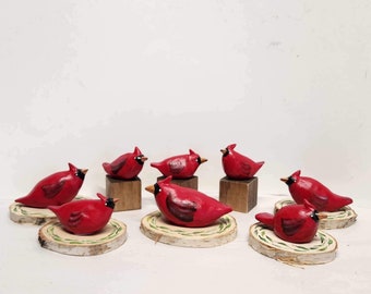May include: Eight hand-painted wooden cardinal figurines on birch wood slices. The cardinals are red with black eyes and beaks. The wood slices are painted with green leaves.