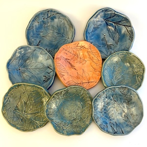 May include: Set of eight ceramic plates with a leaf design. The plates are in shades of blue and green with one plate in a peach color.