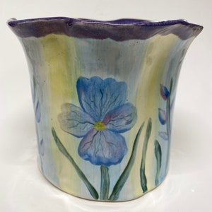 May include: A ceramic planter with a scalloped rim, painted with blue flowers and green leaves on a yellow and blue striped background.