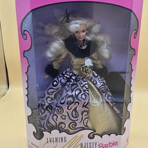 以下が含まれることがあります： Evening Elegance Series Special Edition Evening Majesty Barbieと書かれた箱に入ったブロンドの人形。人形は黒いファーのトリミングが施されたゴールドのボディスと、黒いペイズリー柄、ゴールドのバラ、黒いファーの袖口があしらわれた紫色のスカートを着用しています。