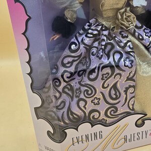 以下が含まれることがあります： 「Evening Majesty」と書かれた箱に入った人形。金色のボディス、黒いファーの袖口、黒と金のペイズリー柄のラベンダー色のスカートを着用。腰には金色の布製のバラがあり、白い髪をしている。パッケージには警告文が記載されている。