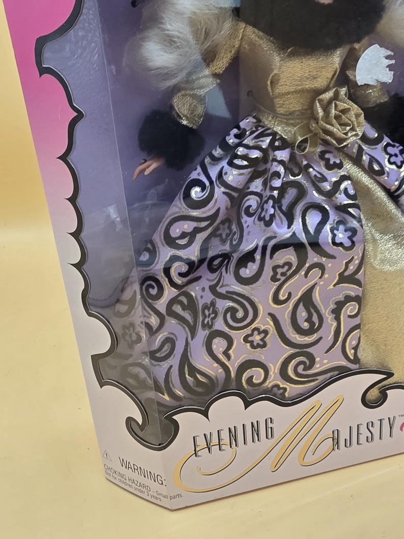 以下が含まれることがあります： 「Evening Majesty」と書かれた箱に入った人形。金色のボディス、黒いファーの袖口、黒と金のペイズリー柄のラベンダー色のスカートを着用。腰には金色の布製のバラがあり、白い髪をしている。パッケージには警告文が記載されている。