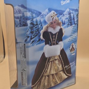 May include: A Happy Holidays Barbie doll in a box, featuring a blonde doll wearing a burgundy velvet gown with white faux fur trim, a matching hat with a snowflake ornament, and a gold skirt, set against a snowy winter landscape background.