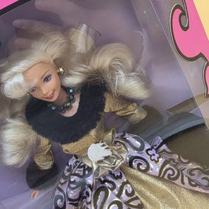 以下が含まれることがあります： ウェーブのかかったブロンドヘアの人形。黒いフェイクファーの襟、ゴールドの長袖ボディス、紫と黒の渦巻き模様にゴールドのアクセントが入ったスカートを着用。暗い色のビーズネックレスを身につけ、箱の中に入っている。