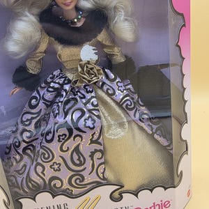 以下が含まれることがあります： Evening Majesty Barbieと書かれた箱に入ったブロンドのバービー人形。人形はダークブラウンのフェイクファーの襟が付いたゴールドのボディスと、パープルとブラックのペイズリー柄のロングスカートを着用しており、ウエストにはゴールドのバラのアクセントが付いています。