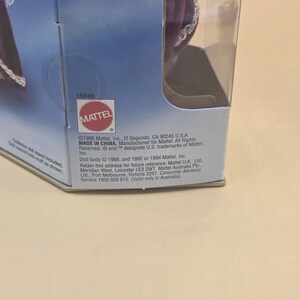 May include: A partial view of a Holidays Barbie doll box featuring a purple velvet garment with silver trim. The packaging includes the Mattel logo, the product number 15646, and printed text detailing the 1996 copyright and manufacturing information.