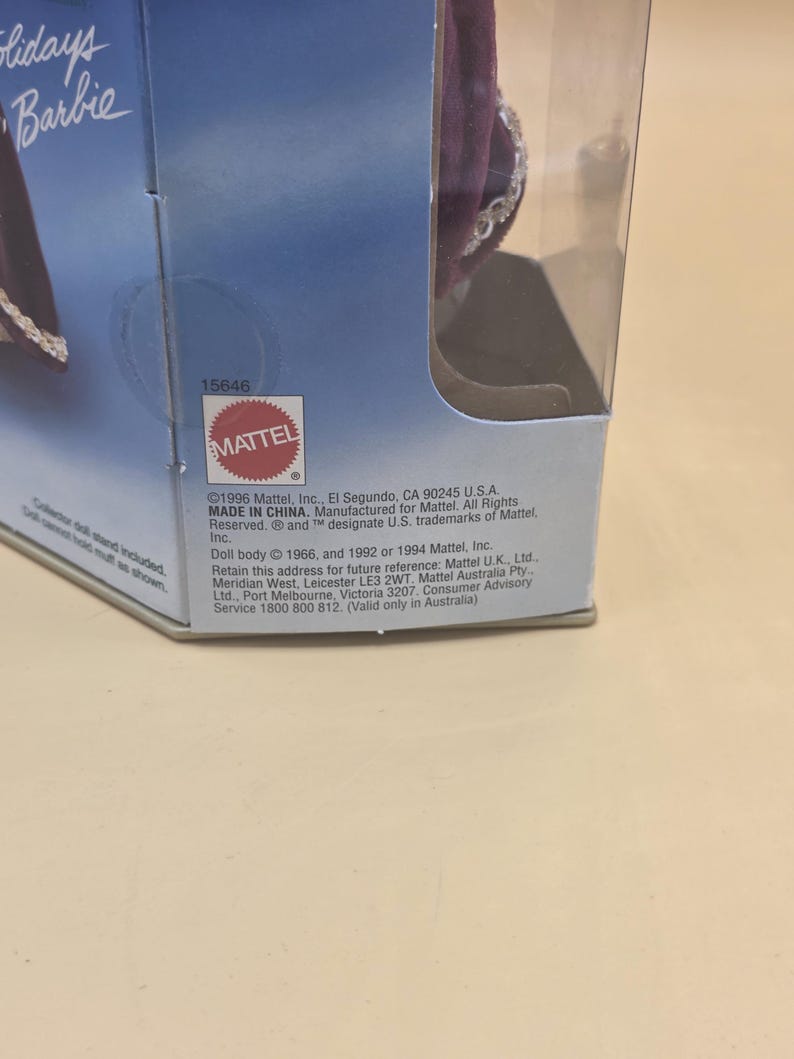 May include: A partial view of a Holidays Barbie doll box featuring a purple velvet garment with silver trim. The packaging includes the Mattel logo, the product number 15646, and printed text detailing the 1996 copyright and manufacturing information.