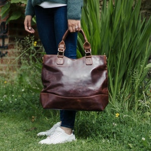 large brown distressed leather tote held in models hand