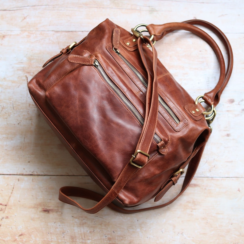 Hampton brown leather handbag showing double front zip pockets, rolled top handles and adjustable crossbody strap