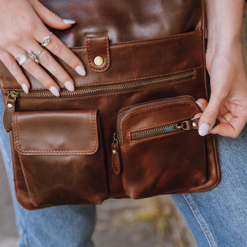 Brown leather crossbody bag with front pockets showing model opening the bag