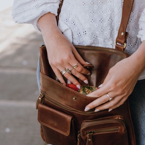 Brown leather crossbody bag with front pockets showing model opening the bag