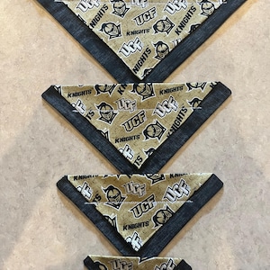 May include: Four triangular bandanas in varying sizes. Each bandana features a tan background with a repeating pattern of the UCF Knights logo and text. The edges are trimmed with a dark gray fabric.