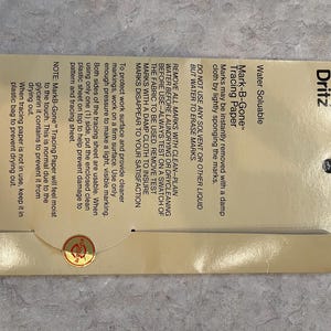 May include: A package of Dritz Mark-B-Gone tracing paper. The package is tan with black text, including instructions for use and the product name. The paper is water-soluble and designed for fabric marking. The package also includes a small gold sticker.
