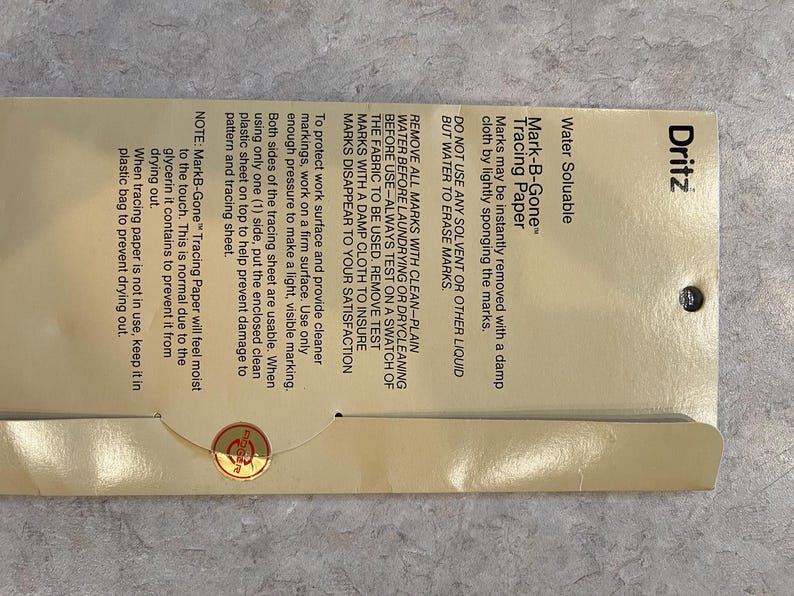 May include: A package of Dritz Mark-B-Gone tracing paper. The package is tan with black text, including instructions for use and the product name. The paper is water-soluble and designed for fabric marking. The package also includes a small gold sticker.