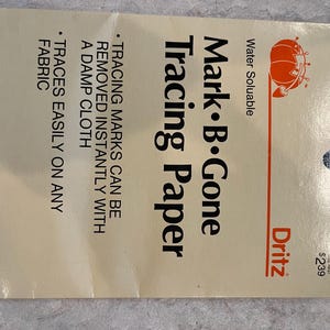 May include: A package of Mark B. Gone Tracing Paper by Dritz. The package is cream-colored with red and black text. The text includes "Water Soluble" and "Tracing Paper". The paper traces easily on any fabric and marks are removed with a damp cloth.