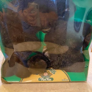 May include: A package of Cabbage Patch Kids Fun Fur, featuring a brown, fluffy material. The packaging is green and yellow, with the Cabbage Patch Kids logo and the words "Fun Fur" printed on the front. The package is sealed in plastic.
