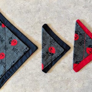 May include: Three triangular bandanas with a horror movie theme. The bandanas are gray with a repeating pattern of a red circle with the word "IT" and the phrase "YOU'LL FLOAT TOO" in black. The edges are trimmed in black and red.