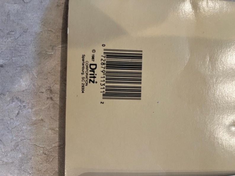 May include: A close-up of a beige product package with a barcode and the text "&copy; 1987 Dritz CORPORATION Spartanburg, SC 29304". The barcode is black and the text is black.