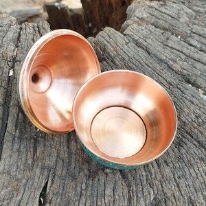 May include: A two-piece copper container with a bowl-shaped base and a matching lid. The interior of both pieces features a polished, reflective copper finish, while the exterior surfaces are finished in a vibrant teal color with decorative gold-toned accents.