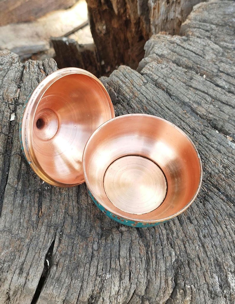 May include: A two-piece copper container with a bowl-shaped base and a matching lid. The interior of both pieces features a polished, reflective copper finish, while the exterior surfaces are finished in a vibrant teal color with decorative gold-toned accents.